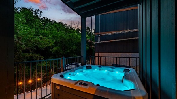 Un jacuzzi en un balcón con vistas a árboles y un atardecer.
