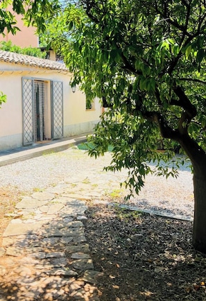 Un cortile pavimentato con un albero, un edificio con tetto in tegole e un cancello in metallo.