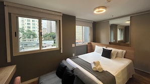 Een hotelkamer met een groot bed, een raam met uitzicht op de stad, een spiegel en een plafondlamp.