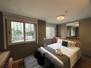 Ein Hotelzimmer mit einem großen Bett, einem Fenster mit Stadtblick, einem Spiegel und einer Deckenleuchte.
