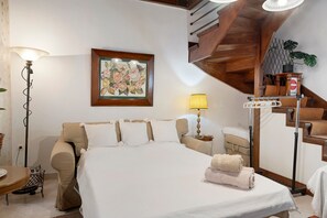 A hotel room with a bed, a nightstand, a lamp, a framed floral artwork, a staircase, and a plant. - Casabella Apartment in Corfu Town with Air Conditioning (Corfu)