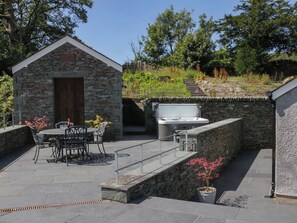 A stone building with a door, a hot tub, and a patio with chairs and a table. - Cragg Cottage (Coniston)