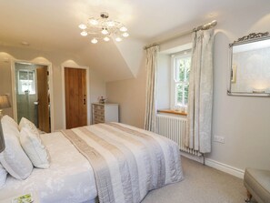 A bedroom with a bed, a dresser, a window with curtains, a radiator, and a chandelier. - Cragg Cottage (Coniston)