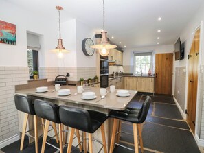 A modern kitchen with a central island, bar stools, a clock, and wooden cabinets. - Cragg Cottage (Coniston)