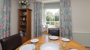 A dining room with a wooden table set for four, surrounded by chairs, and a bookshelf with decorative items. - Cragg Cottage (Coniston)