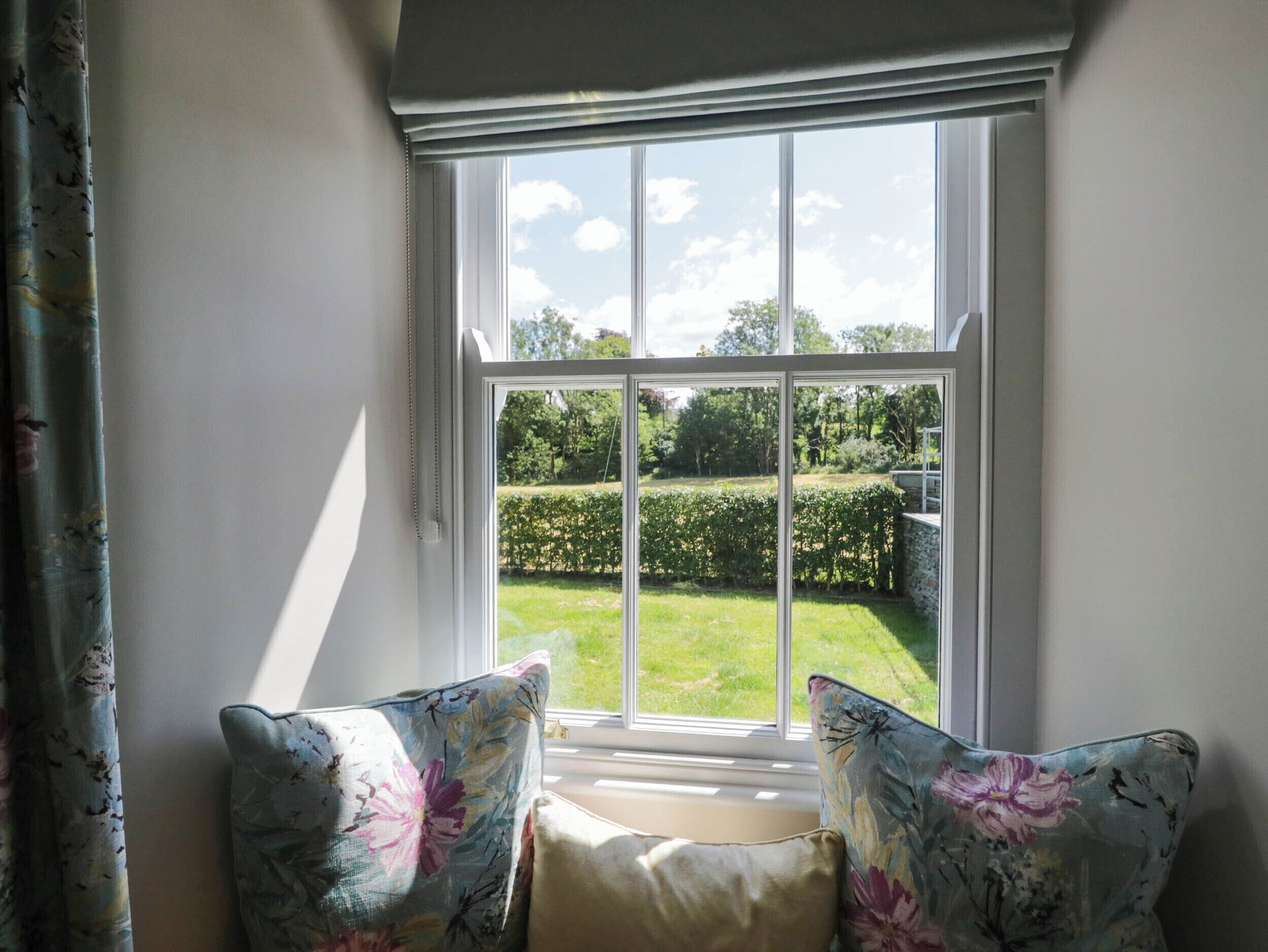 A room with a large window, a bench, and two floral cushions.