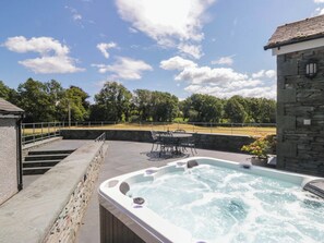 A hot tub with a stone wall and a patio area with outdoor furniture. - Cragg Cottage (Coniston)