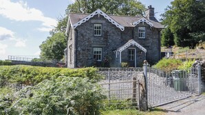 A stone house with a traditional design, featuring a gated entrance and a stone staircase leading to the main door. - Cragg Cottage (Coniston)