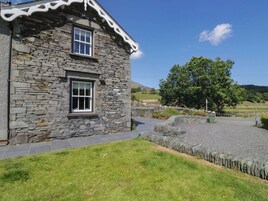 A stone building with two windows, a paved driveway, and a grassy area.