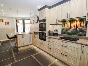 Eine moderne Küche mit Holzschränken, einem Backofen, einer Spüle und einem dekorativen Wandgemälde mit Waldmotiv.