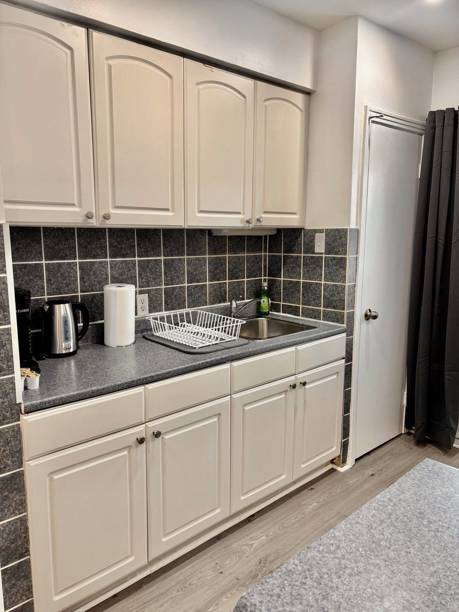A kitchen with white cabinets, a granite countertop, a coffee maker, and a dish rack.