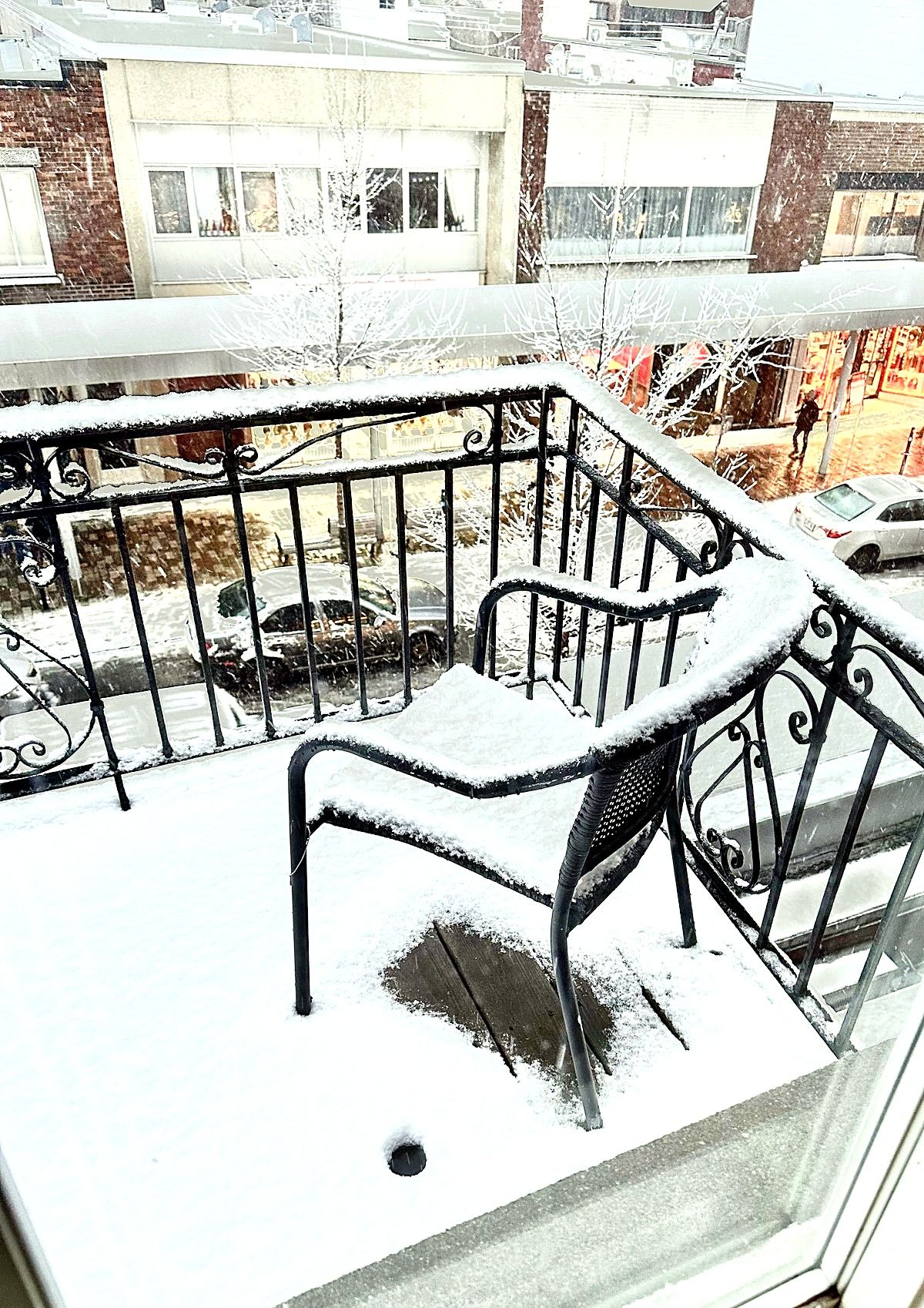 Área externa coberta de neve, com grade de metal e um banco.