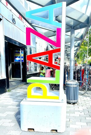 Une sculpture abstraite aux couleurs vives, composée de formes géométriques, se dresse devant un bâtiment dont la façade est vitrée.
