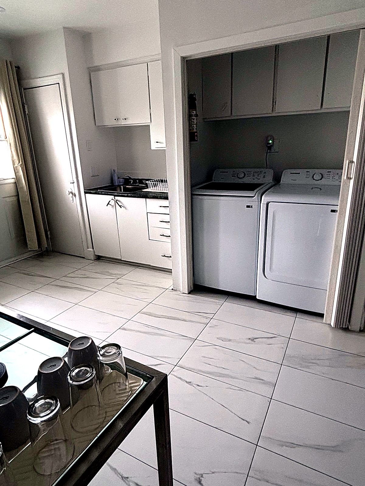 A laundry room with a washing machine and dryer, a small kitchen area with a stove, and a tiled floor.