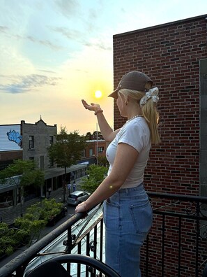 A person standing on a balcony overlooking a street with buildings and a sunset. - Clean and pleasant apartment 8 (Montréal)