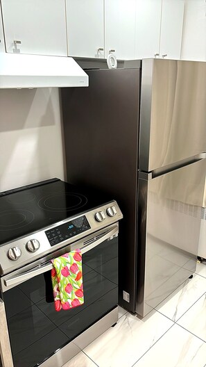 A kitchen with a black stove, stainless steel refrigerator, and white cabinets. - Clean and pleasant apartment 8 (Montréal)
