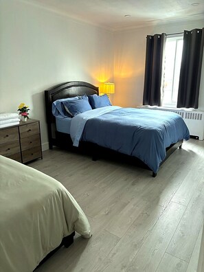 Quarto com cama, mesa de cabeceira, abajur e janela com cortinas.