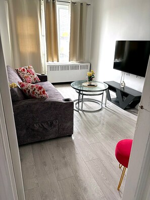 A living room with a sofa, a small round table with a vase, a flat-screen TV, and a red chair. - Clean and pleasant apartment 8 (Montréal)