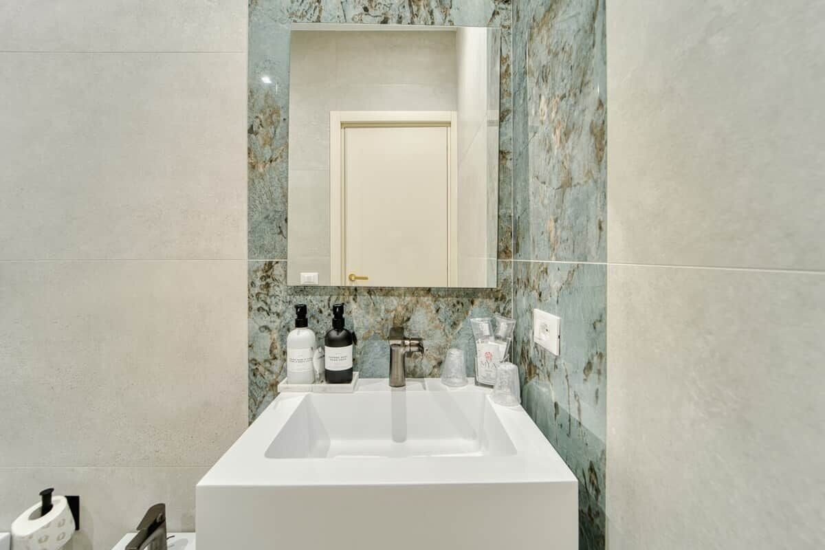 Un bagno con un lavabo bianco, una schiena di marmo e uno specchio sopra.
