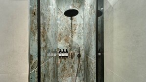 A shower with a marble wall, a handheld showerhead, and a set of bottles likely containing shampoo or conditioner. - Deluxe Double Room (Rome)