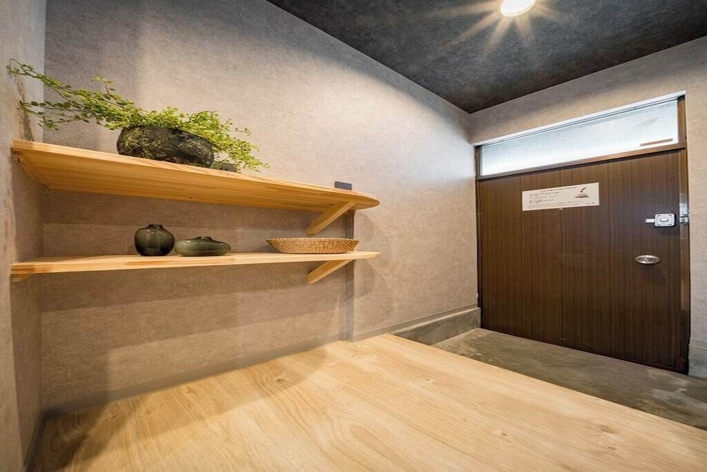 A room with a wooden table, two wooden shelves with decorative items, a potted plant, and a door with a sign.