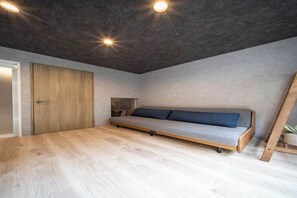 Een moderne kamer met een houten vloer, een grijze bank, een houten deur en een plafond met inbouwverlichting.