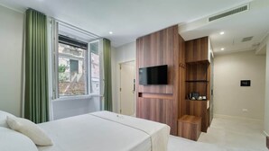A hotel room with a bed, a TV mounted on a wooden panel, and a window with curtains.