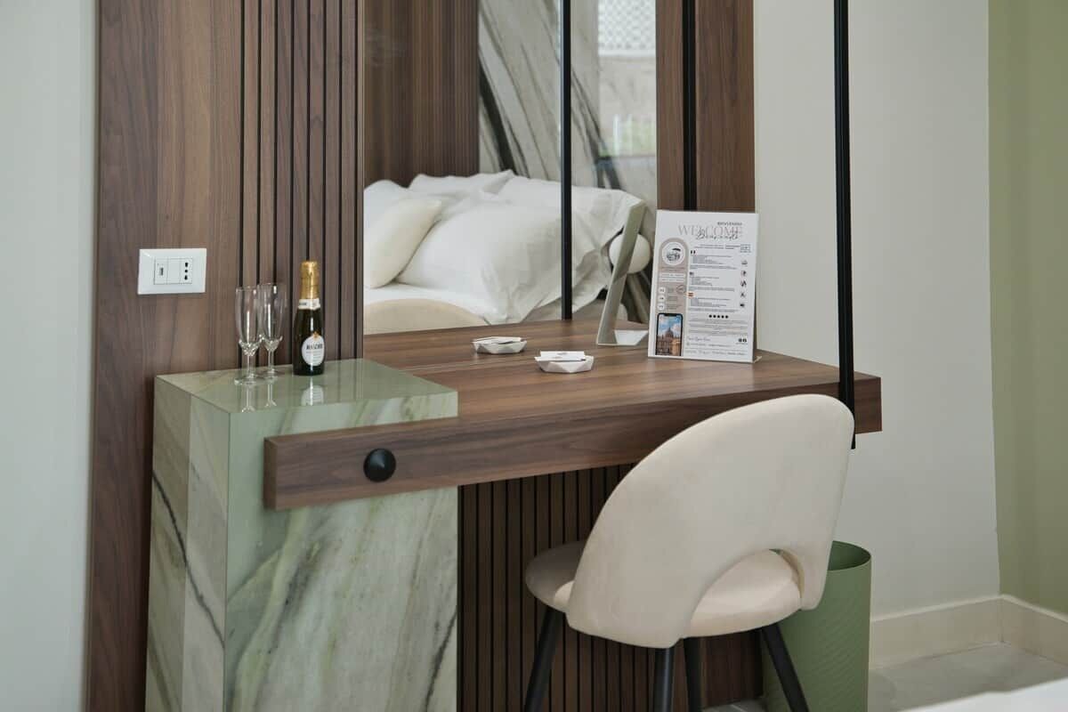 Habitación de hotel con un escritorio de madera, una silla, una botella de vino, copas y un menú sobre la mesa.