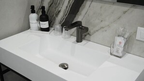 A bathroom with a white sink, a mirror, and toiletries including a bottle of hand soap and a bottle of shampoo.