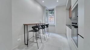 A modern kitchen with a bar area, two bar stools, a built-in oven, and a window with a view of the outside.