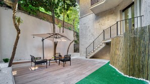 A patio with a wooden deck, a green artificial turf area, and a staircase leading to an upper level.