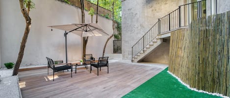 A patio with a wooden deck, a green artificial turf area, and a staircase leading to an upper level.