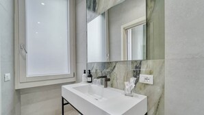 A modern bathroom with a large mirror, white sink, and marble backsplash.