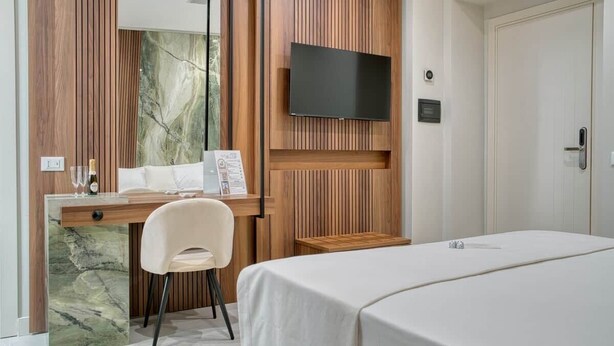 A hotel room with a bed, a desk with a chair, a television, and a wooden panel wall.