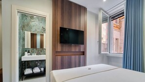A hotel room with a bed, a mounted TV, a bathroom with a sink and mirror, and a window with curtains.