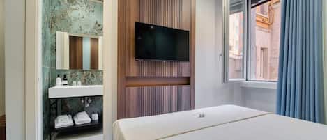 A hotel room with a bed, a mounted TV, a bathroom with a sink and mirror, and a window with curtains.
