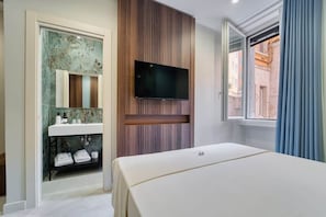 A hotel room with a bed, a mounted TV, a bathroom with a sink and mirror, and a window with curtains.