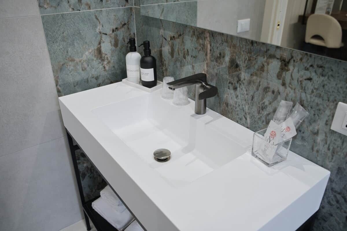 Un bagno moderno con un lavandino bianco, un rubinetto nero e uno schienale in marmo.