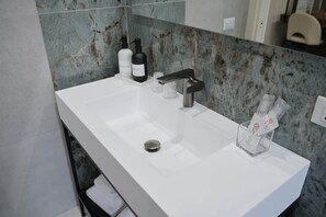 Een moderne badkamer met een witte wasbak, een zwarte kraan en een marmeren spatwand.