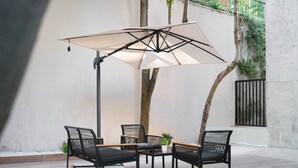 An outdoor patio with a table and chairs, a large umbrella, and a wall with a gate.