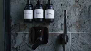 A bathroom with a shower, a handheld showerhead, and three bottles of body care products.