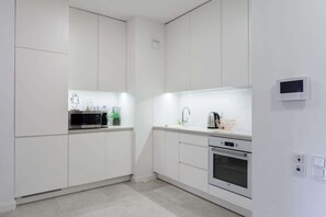 Eine moderne Küche mit weißen Schränken, einer eingebauten Mikrowelle, einem Wasserkocher und einem kleinen Backofen.