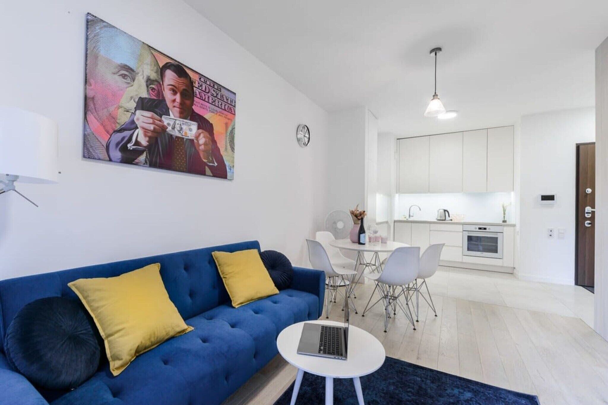 A modern living room with a blue sofa, a small white table, and a kitchen in the background.