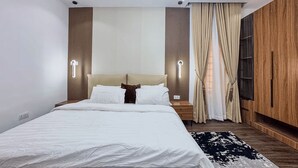 Un dormitorio moderno con una cama, mesitas de noche, lámpara de pared, ventana con cortinas y un armario de madera.