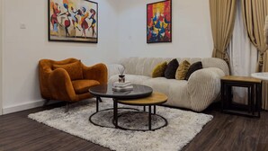 Una sala de estar con un sofá, un sillón, una mesa de centro y dos cuadros abstractos.