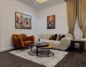 A living room with a sofa, armchair, coffee table, and two abstract paintings. - Exclusive 1-Bedroom in Victoria Island with Pool, Fast Wi-Fi & 24/7 Power (Lagos)