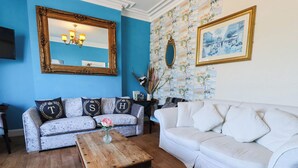 Un salon avec deux canapés, une table basse, un miroir et un mur recouvert d’un papier peint à motifs.