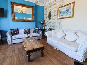 A living room with two sofas, a coffee table, a mirror, and a wall with patterned wallpaper. - The Skegness Hotel (Skegness)
