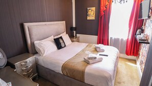 Une chambre d’hôtel avec un lit, une table de chevet, une lampe, un téléviseur et une fenêtre avec des rideaux.