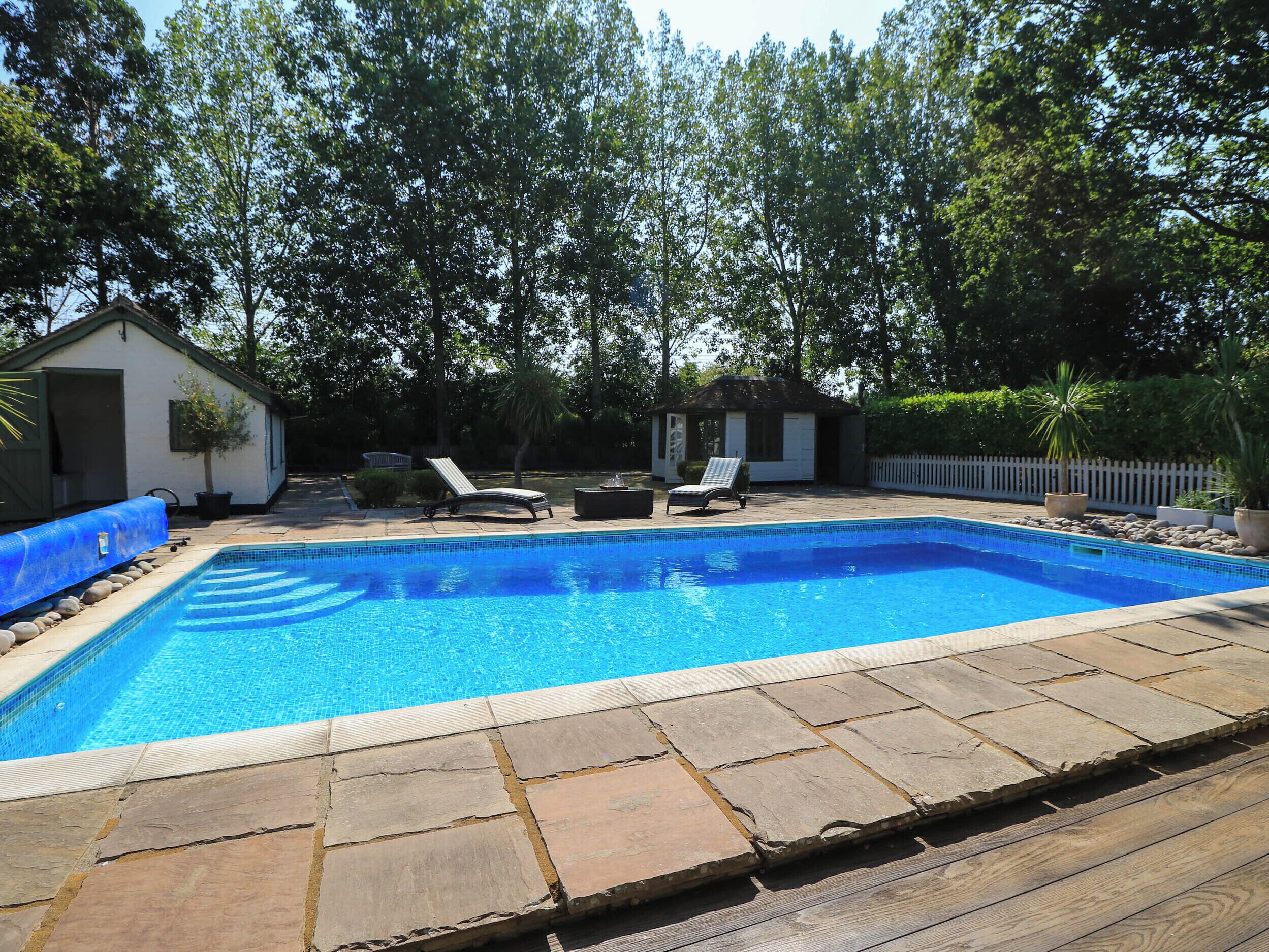 A rectangular swimming pool with a tiled edge, surrounded by a wooden deck and stone tiles.